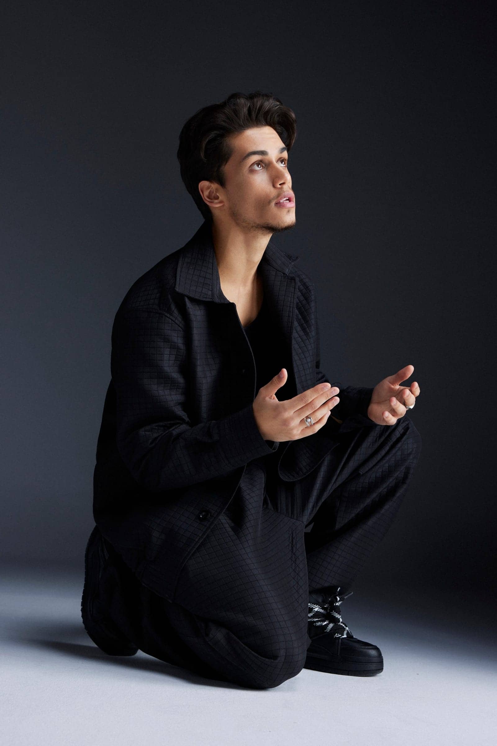 Harris J kneeling in black, hands raised, looking upwards